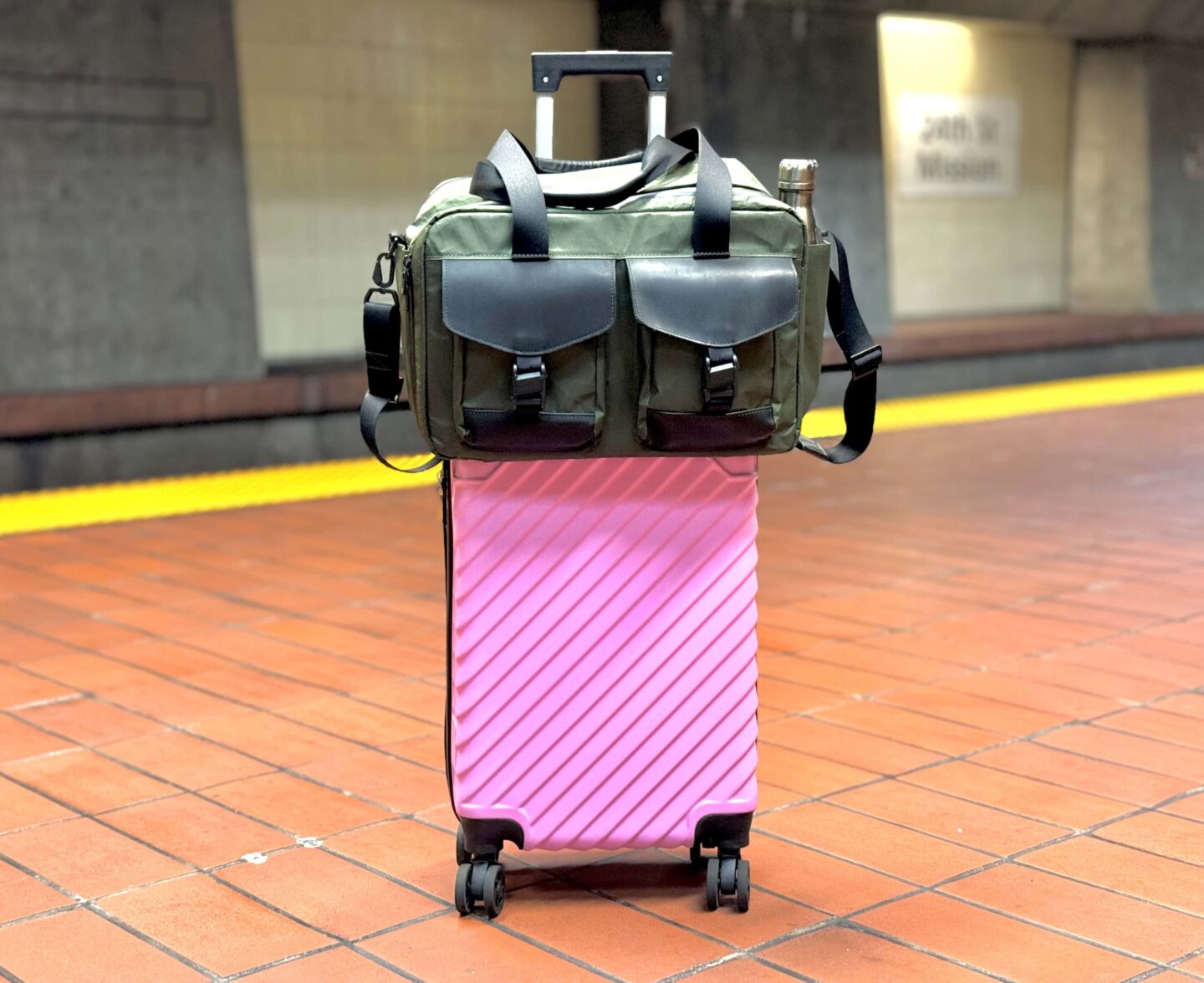 WaterField Designs X Air Duffel on pink luggage WaterField Designs X-Air Duffel in olive green sitting atop a bright pink rolling suitcase on a BART platform in San Francisco.